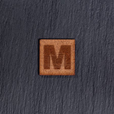 Photo for Capital Letter In Square Wooden Tiles - Letter M, On Black Stone Background. - Royalty Free Image