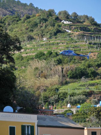 Foto de Monrerosso al mare, Italia - 04 05 2023: Un helicóptero transporta y deja una bolsa grande que contiene materiales de construcción para un sitio inaccesible por carretera. - Imagen libre de derechos