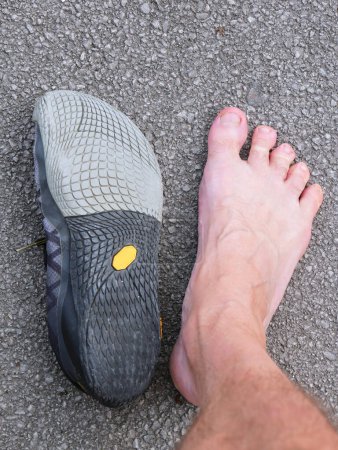Foto de Pie de hombre con dedos extendidos cerca de un zapato descalzo. Para el concepto de caminar descalzo o con zapatos descalzos, para tratar o prevenir el dolor de espalda. - Imagen libre de derechos