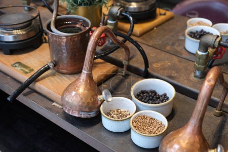 Foto de Pequeños alambiques de cobre y equipo de destilación dispuestos en una mesa decorada. - Imagen libre de derechos