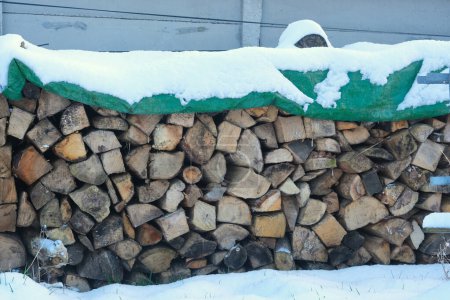 Photo for Reserve of firewood, under a green tarp, covered with snow. - Royalty Free Image