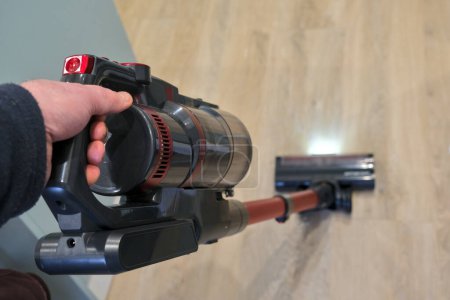 Top view of a hand holding a stick vacuum cleaner. The body is clear and the head is blurred.