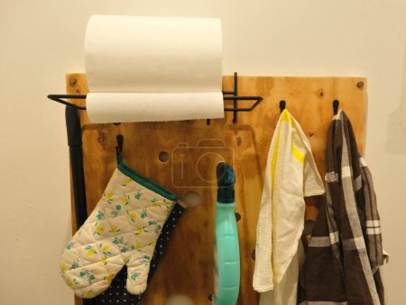 Panel de madera contrachapada, fijado a una pared blanca, sujetando paños, toallas de papel y spray desinfectante.