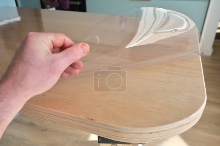 Nappe de protection en plastique transparent, sur une table de cuisine en contreplaqué.