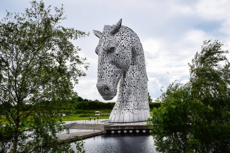 Téléchargez les photos : Falkirk, Royaume-Uni - 5 juillet 2023 : La tête de cheval en acier Kelpies encadrée d'arbres. Statue d'Andy Scott. Helix Park, Écosse. gaélique écossais : Chaque-Uisge. - en image libre de droit