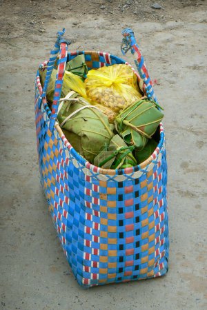 Colorful woven shopping bag filled with groceries wrapped in banana leaves. Ecological basket alternative to plastic packaging bags. Southeast Asia.