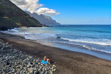 Couple on black sand beach enjoying the scenic north coast of Tenerife, wild Canary Islands landscape, beauty of Spain, travel Europe