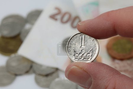 Detalle de una moneda, corona checa entre los dedos, dinero en el fondo
