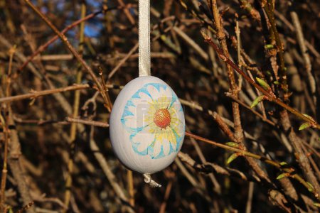 Easter egg decorated with napkin technique hung on a ribbon on spring twigs of a bush