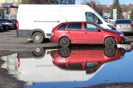 Téléchargez les photos : Parking après la pluie - voitures garées et leur reflet dans une flaque d'eau - en image libre de droit