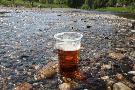 Ein Becher Bier im Wasser des Flusses