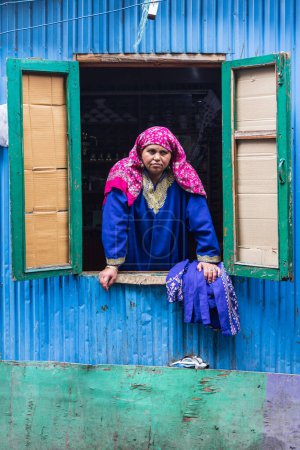 Téléchargez les photos : Hazratbal, Srinagar, Jammu-et-Cachemire, Inde. 30 octobre 2022. Femme penchée par une fenêtre dans une maison bleue. - en image libre de droit