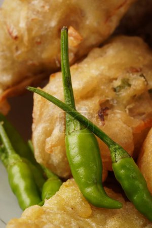 Green bird's eye chili, known for its spicy kick, often accompanies snack foods like fritters.