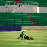 A groundskeeper tends to the lush green turf at a vibrant soccer stadium, adorned with colorful spectator seats