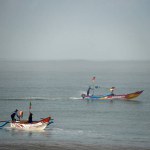 Two fishing boats, each with two fishermen aboard, operating along the shoreline in search of fish. The boats gently navigate the coastal waters, reflecting the traditional livelihood of the local community.