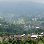 A village nestled at the base of Mount Sumbing in Central Java, featuring homes and farmland laid out along the hilly contours, creating a picturesque and harmonious rural landscape.