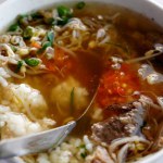 A hearty beef soup or Soto typically enjoyed for breakfast, filled with rice, chopped scallions, bean sprouts, tender beef slices, and a flavorful clear broth.