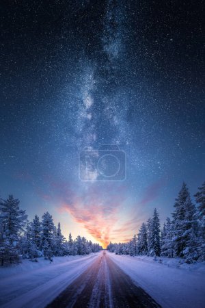 Foto de Camino que conduce hacia el colorido amanecer entre los árboles cubiertos de nieve con la épica vía láctea en el cielo - Imagen libre de derechos