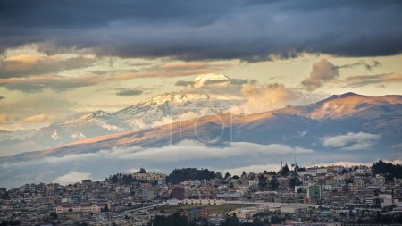 Téléchargez les photos : Le volcan Cayambe dominant la ville de Quito et illuminé par le soleil du soir avec un ciel nuageux orageux - en image libre de droit