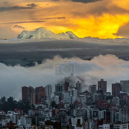 Foto de Parte noreste de la moderna ciudad de Quito y volcán Antisana (5758m) retroiluminada por una magnífica luz dorada con un banco de nubes y niebla que cubre el valle y la parte oeste de la ciudad de Quito - Imagen libre de derechos
