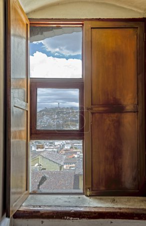 Téléchargez les photos : Gros plan d'une fenêtre en bois à l'intérieur du monastère d'Agustinas à Quito montrant une vue sur la vieille ville coloniale avec la colline de Panecillo abritant la statue de la Vierge de Quito - en image libre de droit