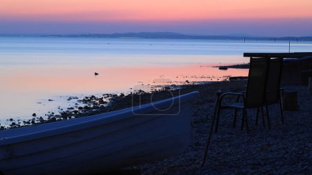 Photo for Sunset on Lake Constance on the coast of Langenargen in Germany with wooden boat and chairs in the foreground - Royalty Free Image