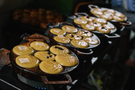 Foto de La leche de coco, la harina, los huevos y las papas se fríen en una sartén de pastel para producir aperitivos tradicionales indonesios conocidos como Kue Lumpur o Mud Cake. - Imagen libre de derechos