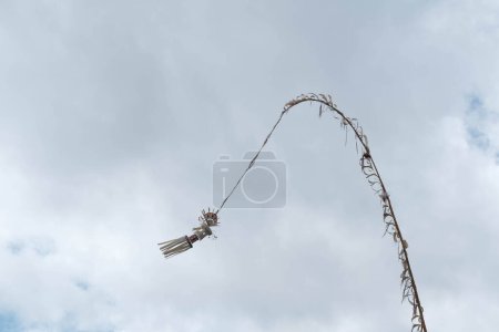 Téléchargez les photos : Une décoration balinaise traditionnelle, un Penjor, balançant dans le vent sur un ciel clair et un fond nuageux - en image libre de droit