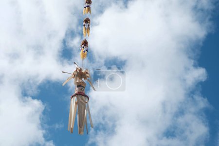 Téléchargez les photos : Une décoration balinaise traditionnelle, un Penjor, balançant dans le vent sur un ciel clair et un fond nuageux - en image libre de droit