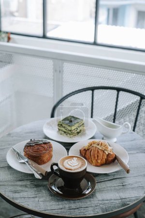 Foto de Una mesa con platos de panadería y tazas de café en ella. Enfocado en la taza de café. Retrato o vertical. Desayuno de la mañana. Fondo borroso. - Imagen libre de derechos