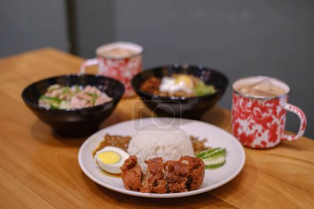 Foto de Un conjunto de cocina malaya contenía Arroz de pollo al vapor, Nasi Lemak, Chili Pan Mee, y dos tazas de té tailandés en una mesa de madera con fondo borroso - Imagen libre de derechos