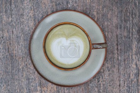 Photo for Flat lay or top view shot of a cup of Matcha Latte with beautiful Latte Art on wooden table - Royalty Free Image
