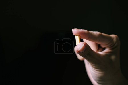 Téléchargez les photos : Une pilule jaune est tenue en pointant du doigt et du pouce. Fond noir isolé. Convient pour la publicité. - en image libre de droit