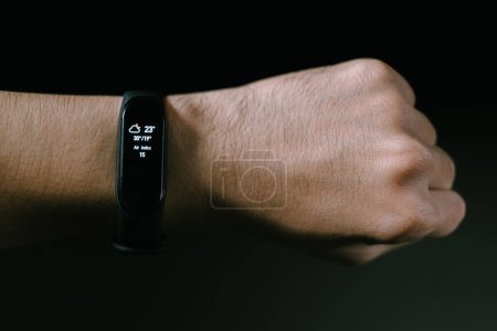 A smartwatch in the hand of men is showing weather, temperature, and air index information. Isolated black background.
