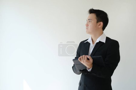 Photo for Young Asian businessman holding a tablet device and looking to his right side. Isolated white background. - Royalty Free Image