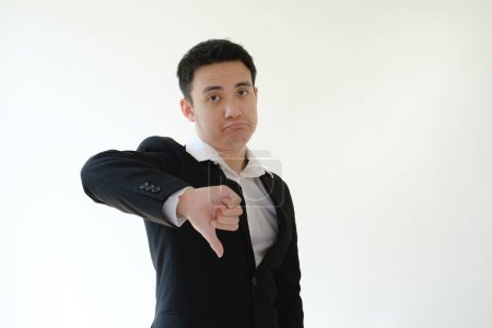 Foto de Joven hombre de negocios asiático con una expresión de aversión a la cara dando su pulgar hacia abajo a la cámara. Fondo blanco aislado. - Imagen libre de derechos