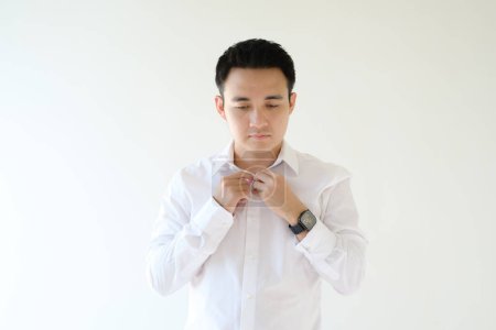 Foto de Un joven asiático abotonándose la camisa blanca. Fondo blanco aislado. - Imagen libre de derechos