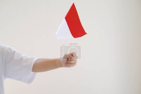 Foto de Una mano de hombre que lleva una camiseta blanca sostiene la bandera de Bendera Indonesia o Indonesia con confianza. Fondo blanco aislado. - Imagen libre de derechos