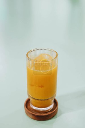 Photo for Portrait or vertical and selective focus shot of a glass of Ice Kunir Asem which is Javanese traditional herbal medicine drinks on isolated sage green pastel table - Royalty Free Image