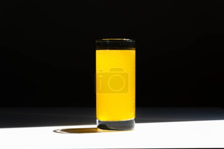 Téléchargez les photos : Un verre d'eau vitaminée C avec des bulles sur table blanche et fond noir - en image libre de droit