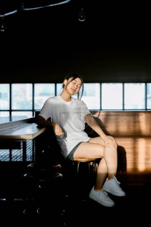 Foto de Una joven asiática sentada en el café tiene una leve sonrisa en la cara y parece tener los ojos cerrados. Retrato o vertical. - Imagen libre de derechos