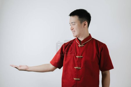 Téléchargez les photos : Visage souriant de l'homme asiatique portant un tissu traditionnel chinois appelé Cheongsam ouvre la main et regarde le côté gauche sur fond blanc - en image libre de droit