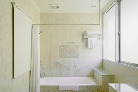 Luxus-Badezimmer mit Badewanne und Krallenfuß-Badewanne unter einem Fenster, das von Marmorfliesenboden und Wand umgeben ist