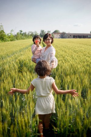 mother and two daughters in summer dresses standing in grain field