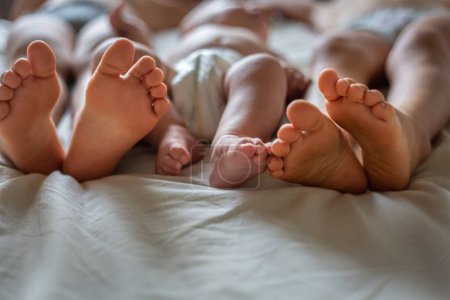 Foto de Pies de dos hermanos mayores y bebé recién nacido en la cama en casa - Imagen libre de derechos