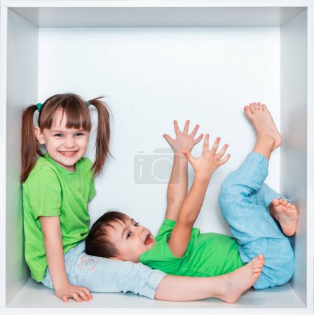 Une fille et un garçon en T-shirts verts jouent ensemble. Enfants sur fond blanc. Enfants dans une niche de meubles blancs. Photo émotionnelle, enfance heureuse, enfants - frère et s?ur.
