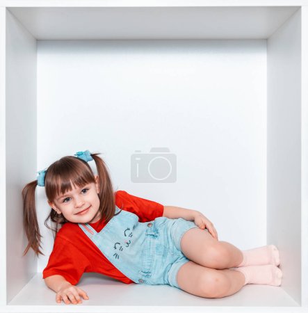 Une petite fille se couche sur le côté et tient une sucette rouge dans sa main. La fille a 3 ans. L'enfant sourit magnifiquement. Bonne enfance.