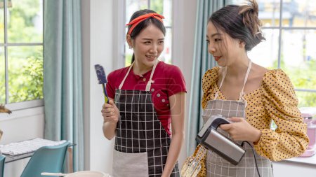Téléchargez les photos : Jeunes femmes travaillant ensemble dans une cuisine pour la boulangerie artisanale. Une dame avec tablier enseigne à un ami comment faire du pain frais à la maison. - en image libre de droit
