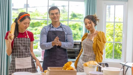 Téléchargez les photos : Partenariat d'affaires entre un homme et deux jeunes femmes dans une boulangerie maison. Formation boulangerie avec des jeunes filles dans une maison - en image libre de droit