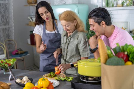 Photo for Young couple working with grand mom to prepare meal at home. Happy family is cooking breakfast with healthy food together - Royalty Free Image